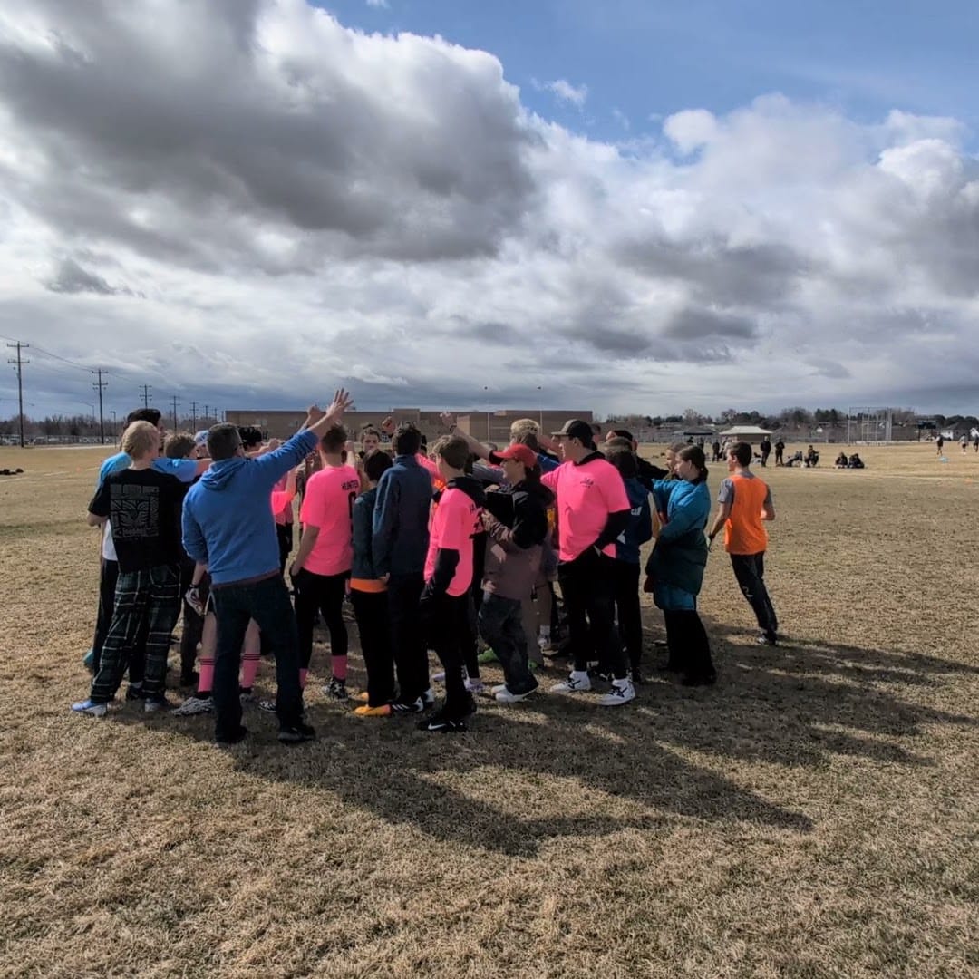 A youth team and their coaches in a huddle on the field.